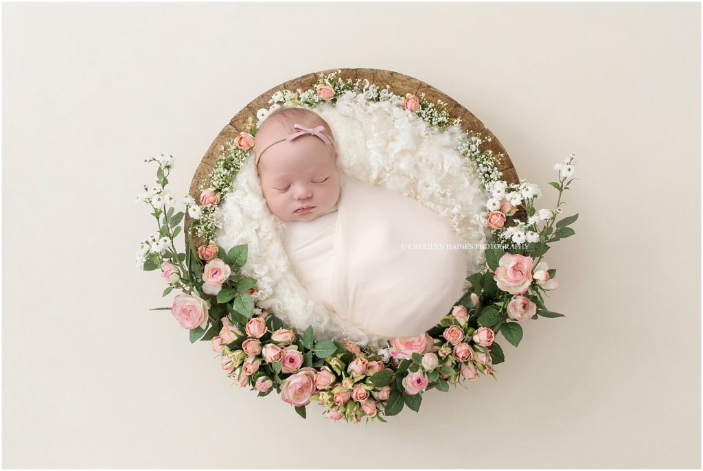 newborn baby swaddled and laying in round basket with pink roses