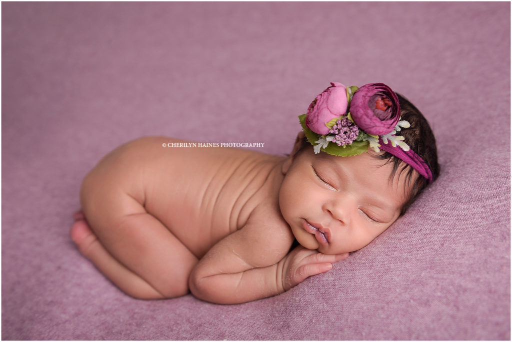 9 day old newborn baby girl photographed laying on lavender blanket while wearing a pink floral headband - portrait by Cherilyn Haines Photography in Baton Rouge, Louisiana