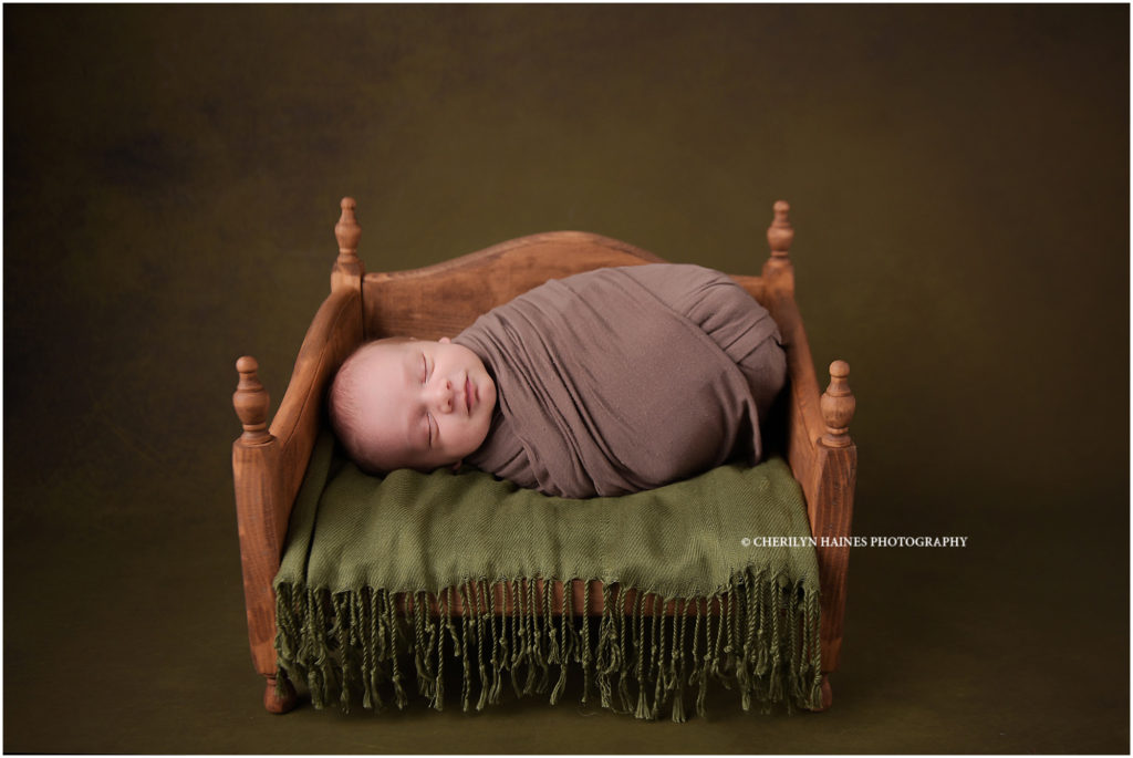 cherilyn haines photography photographs a newborn baby laying on brown wooden daybed on olive green backdrop