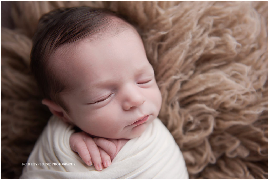 10 day old newborn baby boy photographed by cherilyn haines photography in baton rouge, louisiana; baby boy swaddled in white swaddle laying on tan rug