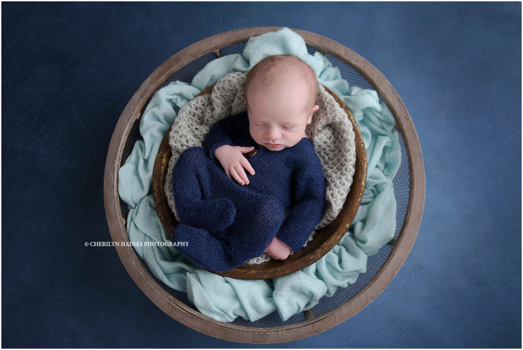 13 day old baby boy photographed in navy knit romper sleeping in brown bowls with light blue blanket; photographed by cherilyn haines photography