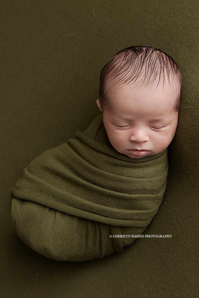 3 week old newborn baby boy photographed in an olive green swaddle laying on an olive green blanket