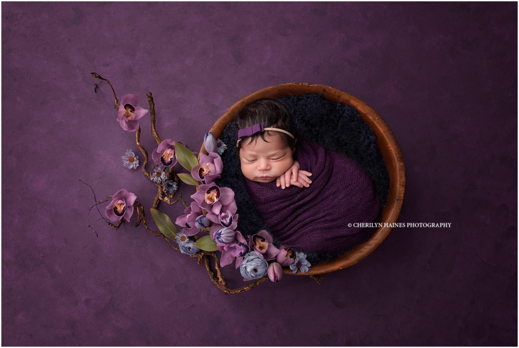 newborn baby girl photographed with purple orchids