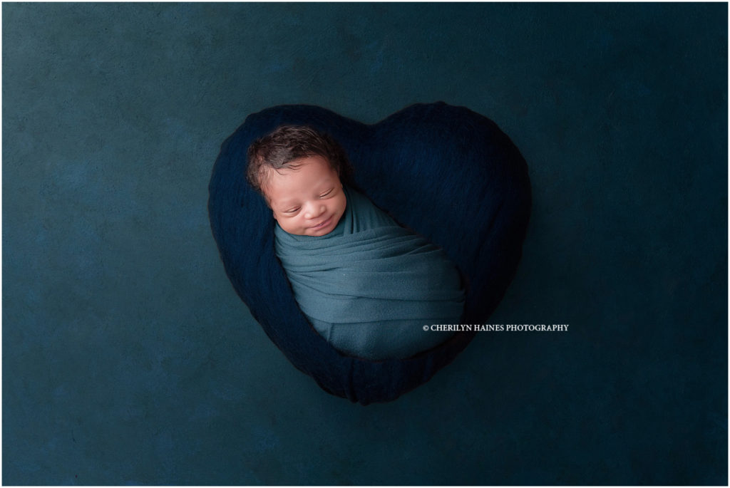 newborn baby boy swaddled in teal, photographed on navy heart