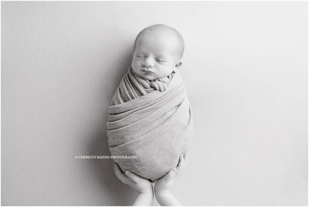 black and white picture of big sister's hands hold newborn baby brother