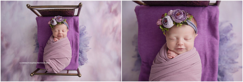 smiling newborn baby girl photographed swaddled in purple laying on tiny bronze bed
